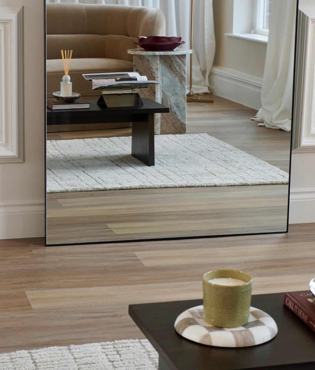 Lower half reflection of arched full-length black frame mirror showing velvet sofa and marble side table
