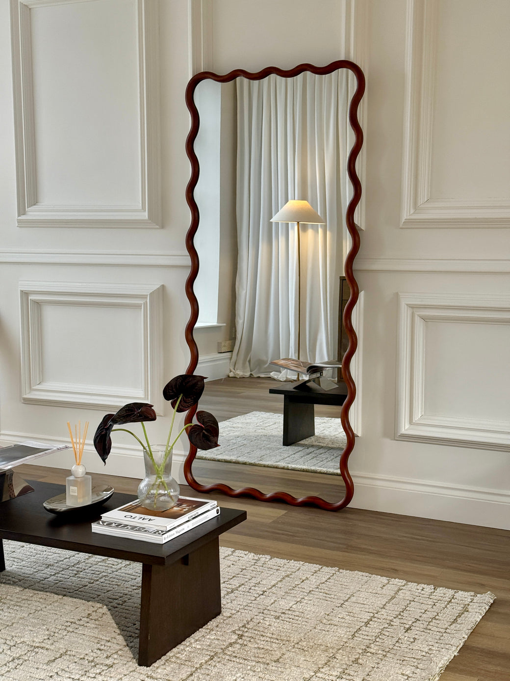 Wavy walnut wood frame full-length mirror beside velvet sofa and coffee table in living room