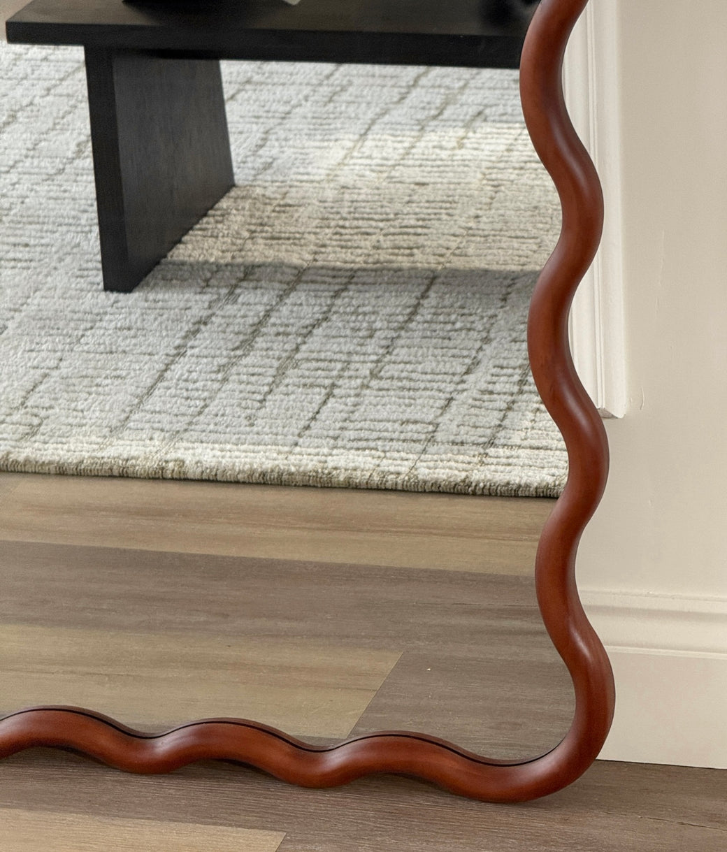 Base detail of sculptural wavy walnut wood frame on full-length floor mirror