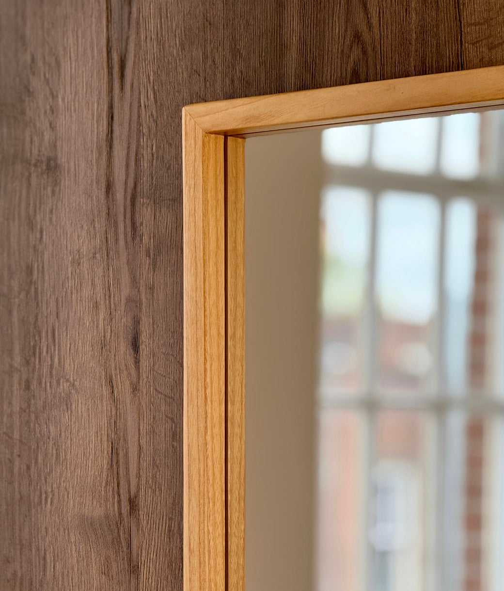 Top corner detail of full-length mirror with natural oak wood frame against white panelled wall