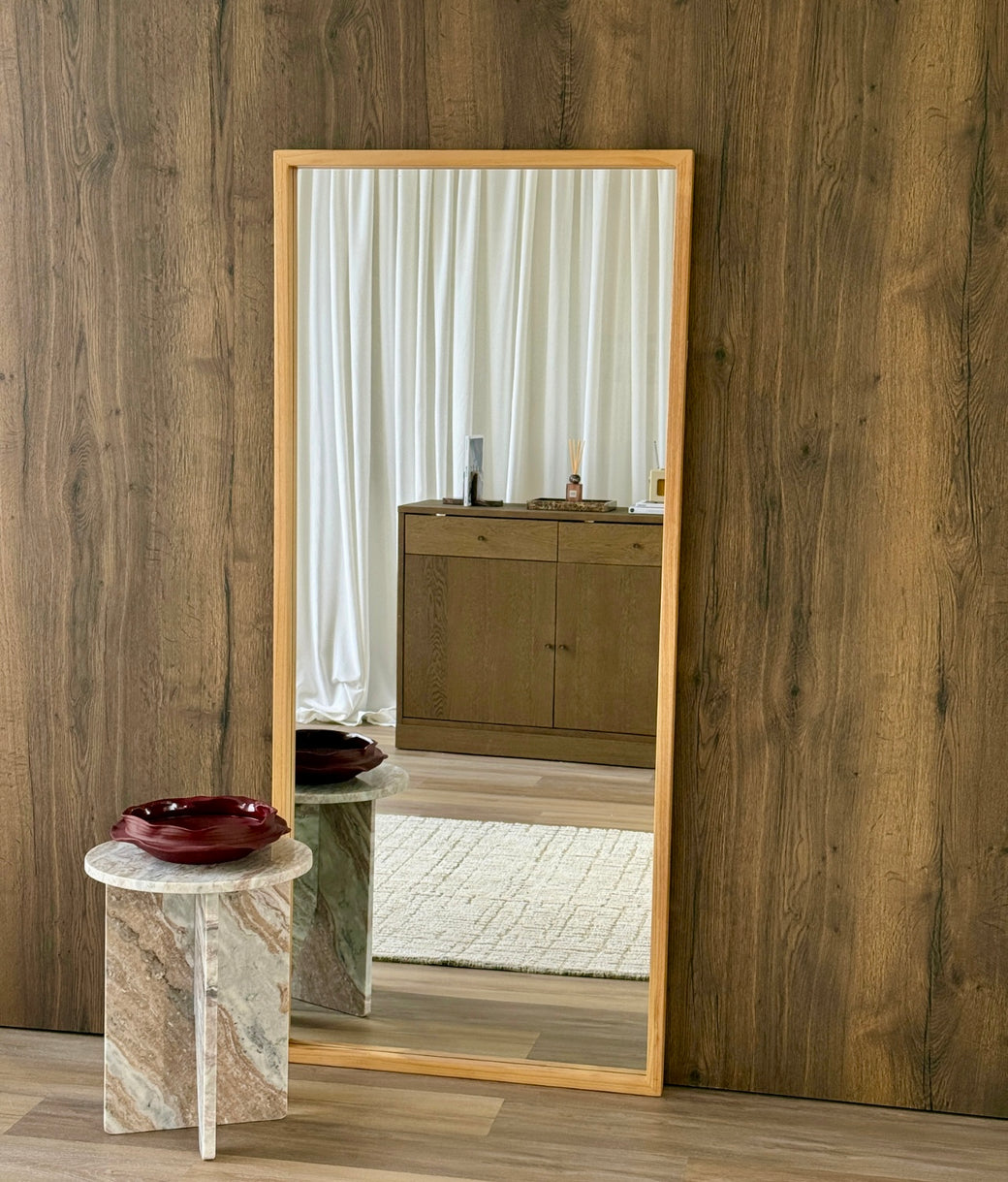Full-length oak frame mirror leaning against dark wood-panelled wall with marble side table