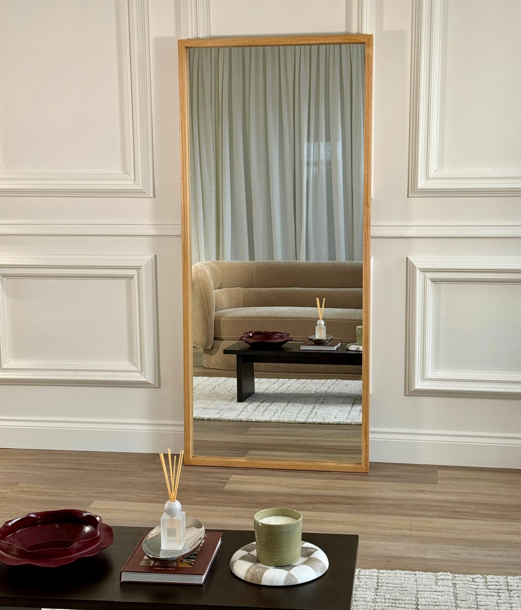 Full-length oak frame mirror leaning against dark wood-panelled wall with marble side table