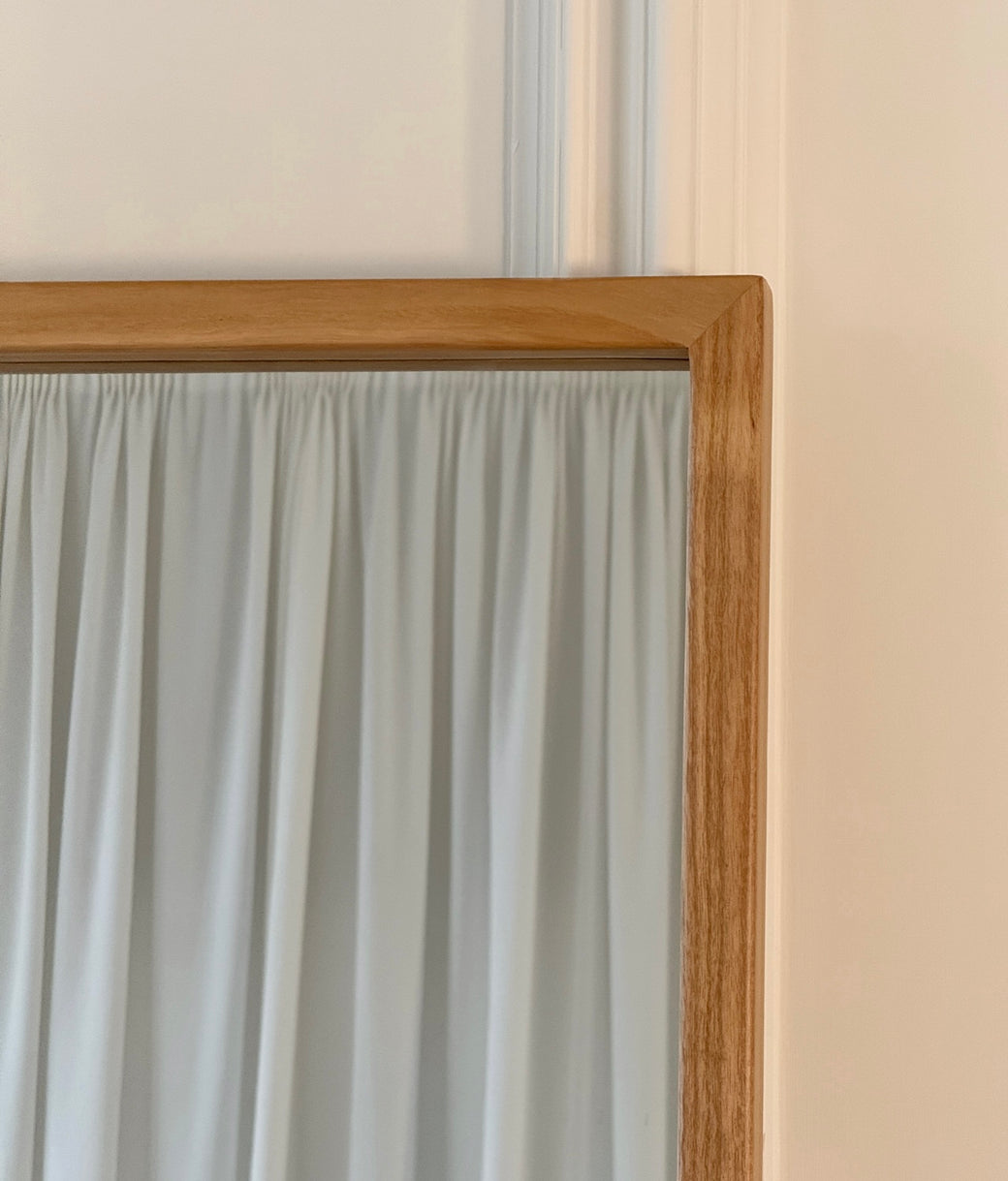 Corner frame detail of full-length natural oak mirror against dark wood-panelled wall