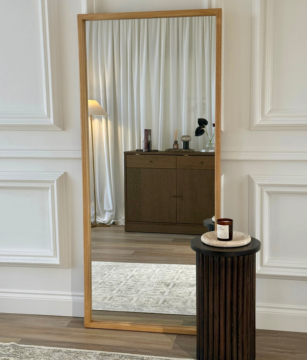 Full-length leaner mirror with natural oak frame leaning against white panelled wall in modern living room
