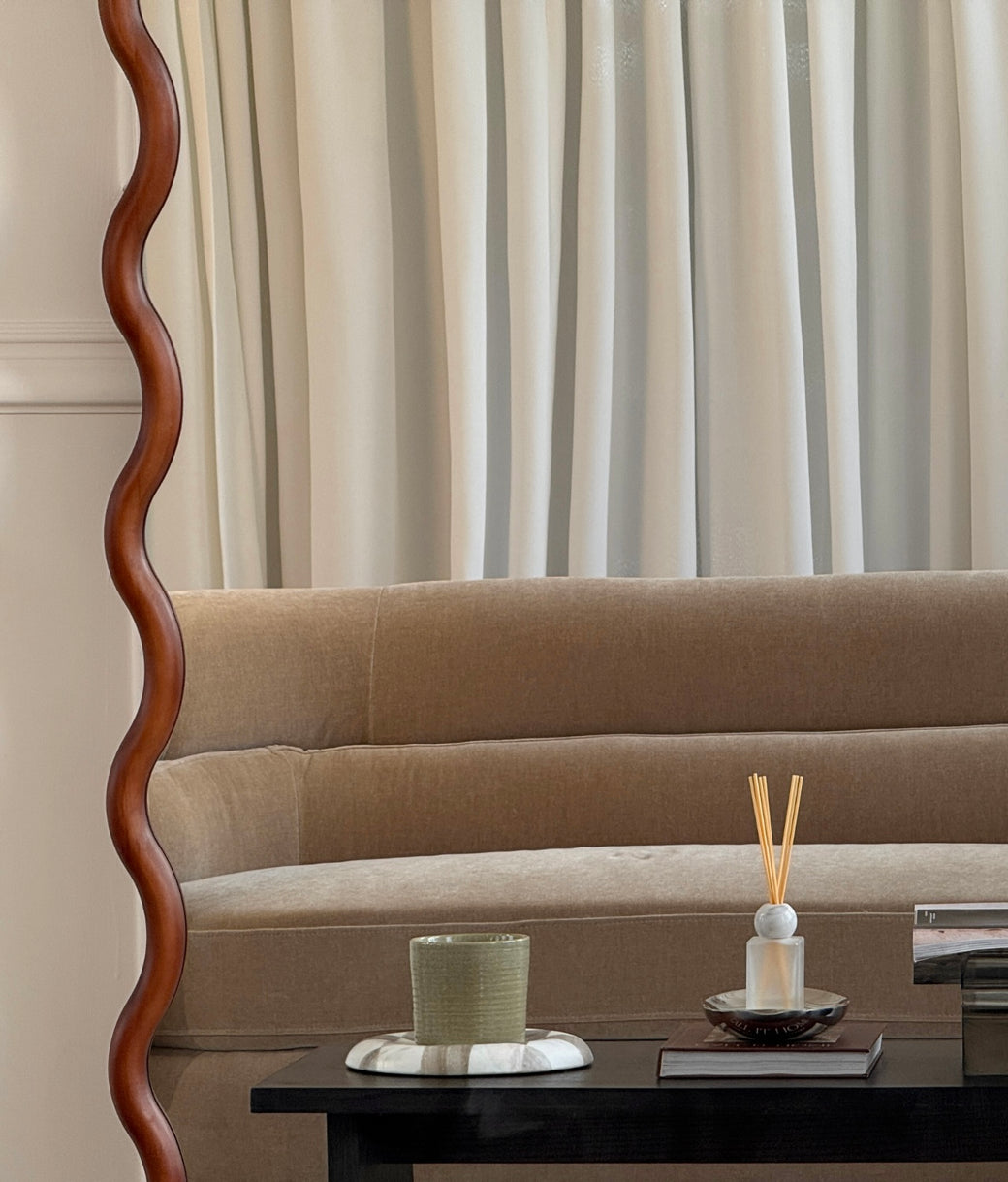 Side detail of wavy walnut wood frame mirror leaning against white panelled wall