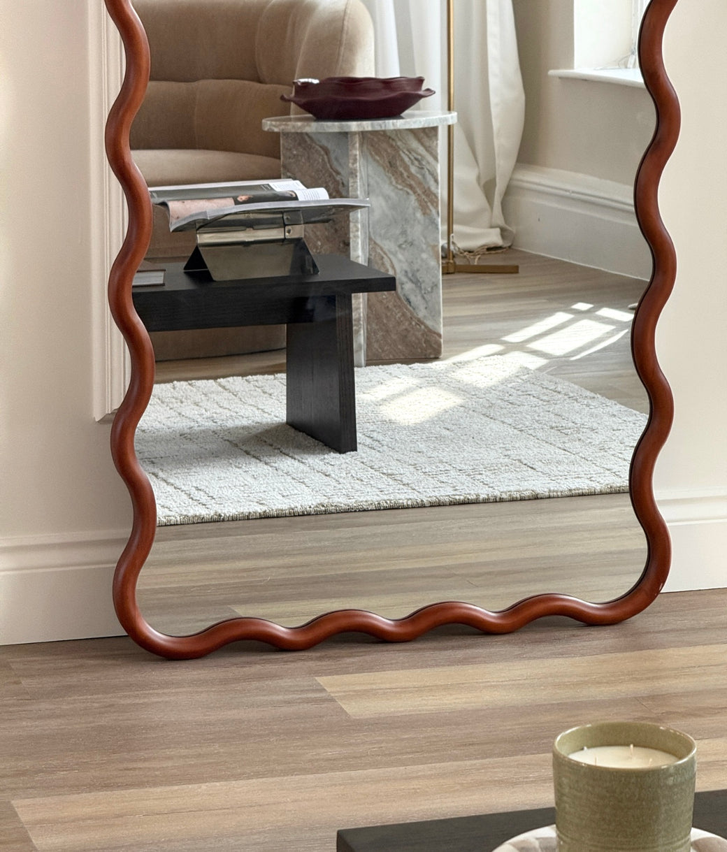 Lower half of full-length wavy walnut mirror showing sculptural frame and living room reflection