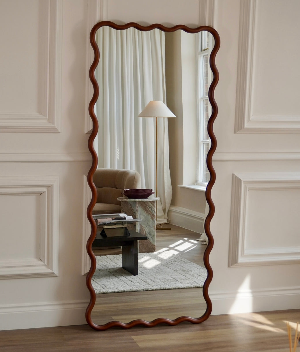 Wavy walnut wood frame full-length mirror beside velvet sofa and coffee table in living room
