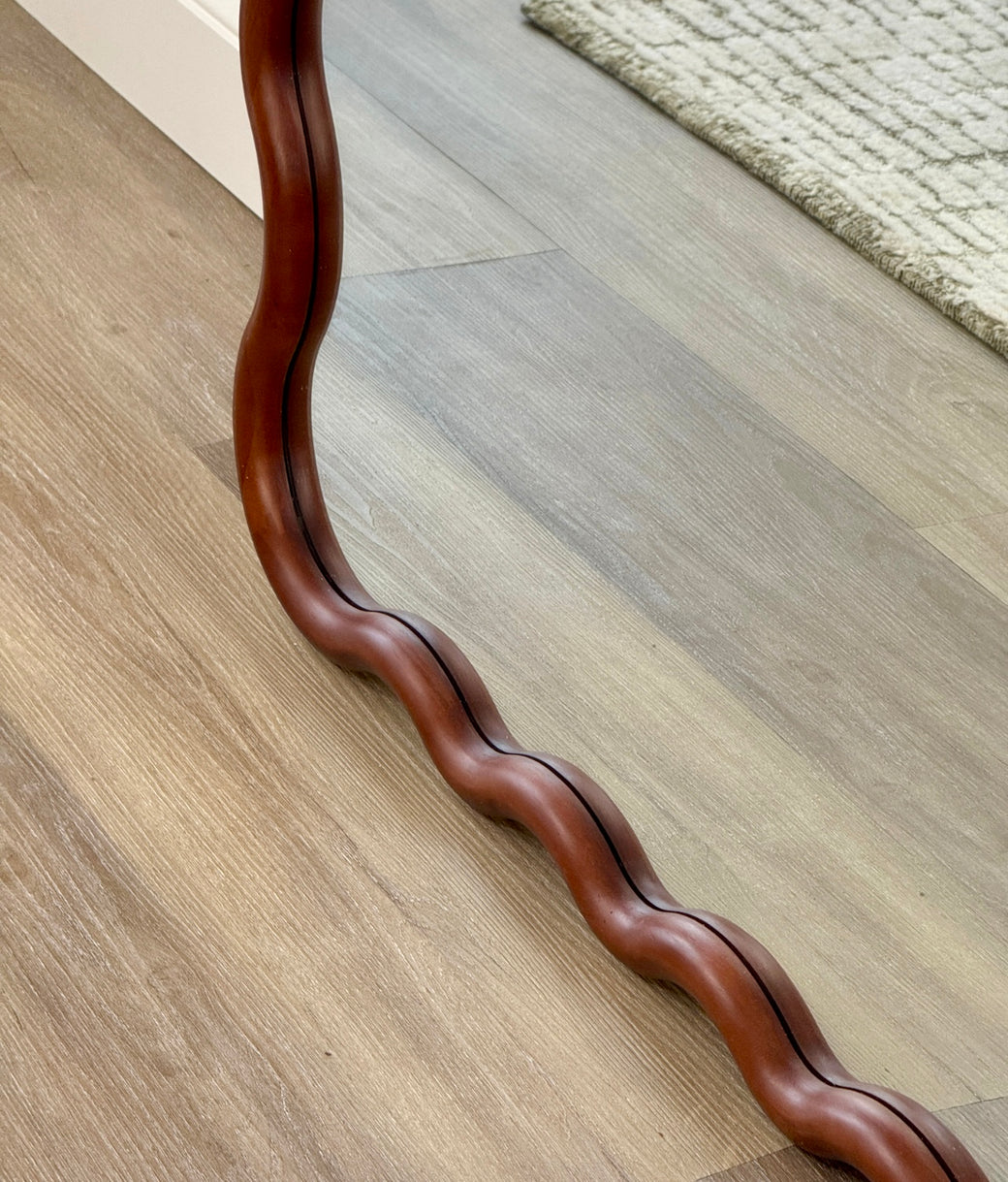Base detail of sculptural wavy walnut wood frame on full-length floor mirror